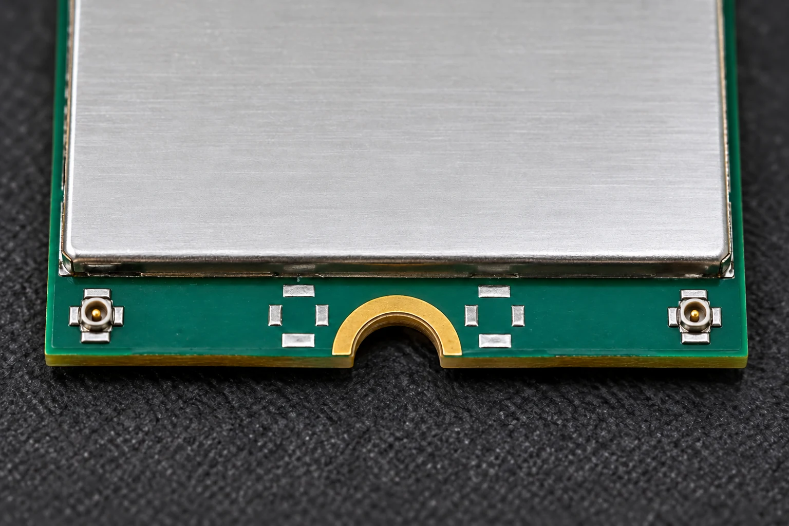 Nahaufnahme eines grünen Elektronikmoduls mit Metallabschirmung und zwei kleinen Antennenanschlüssen.